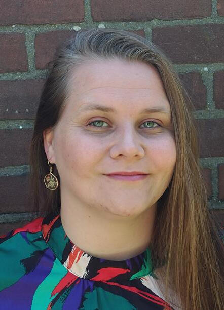 img src="Portrait of poet Carina van Os, in a colourful dress with a brick wall background"